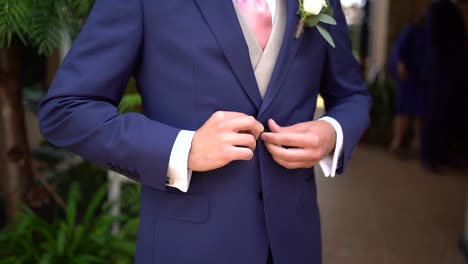 slow motion shot of groom fastening the buttons on his blue jacket suit, tracking motion