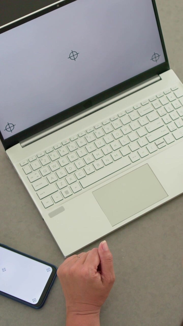 Vertikales Video: Eine Hand dreht das Handgelenk über einem Laptop-Pad am Schreibtisch und richtet sich am Telefon aus.