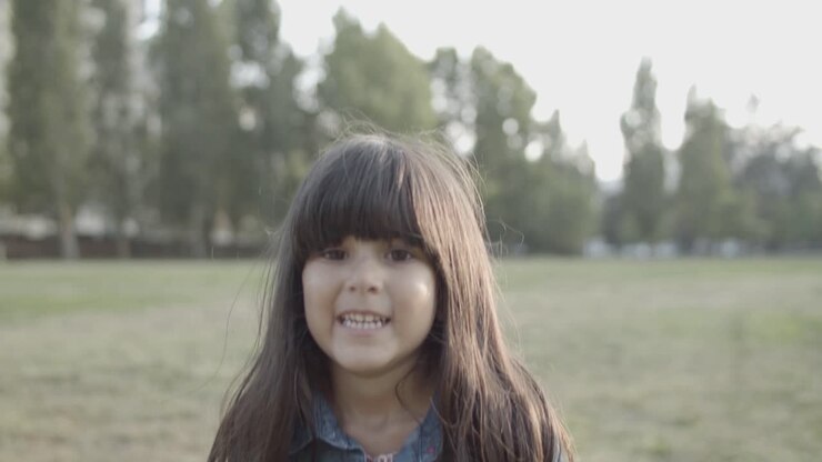 Retrato de una linda niña latina de pie en el parque, sonriendo a la cámara y saltando