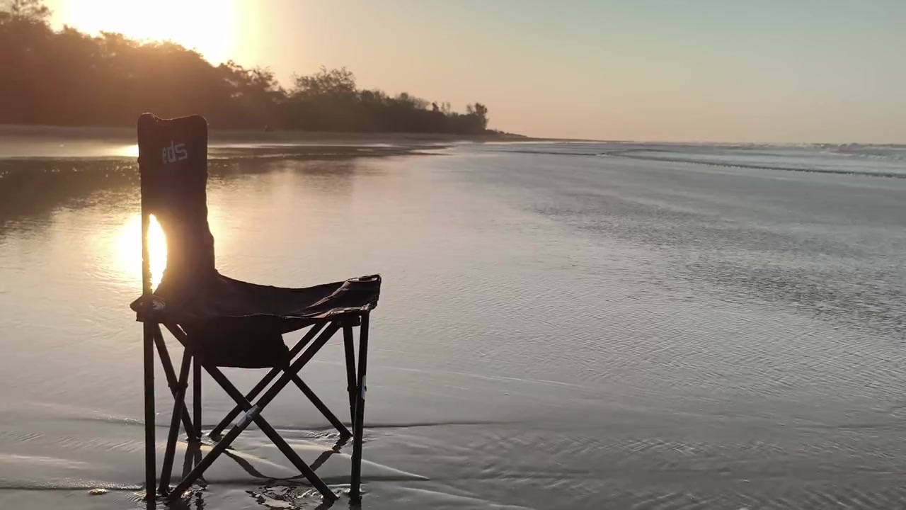 Sedia pieghevole vuota su una spiaggia sabbiosa al tramonto