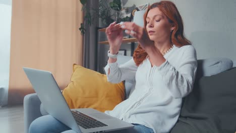 tired adult caucasian woman freelancer works sits on sofa with laptop on lap