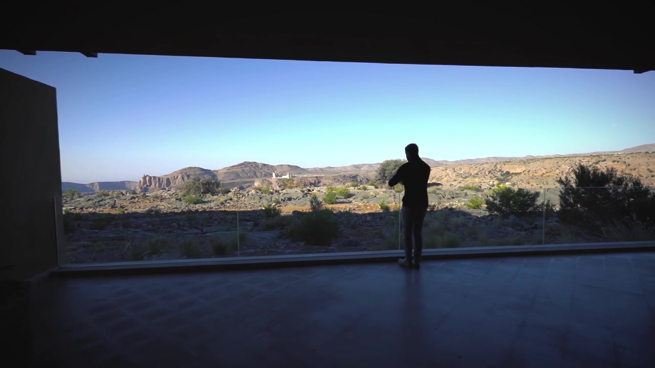 Dark silhouette of a man passes by and enjoys the view from a hotel complex onto a desert landscape