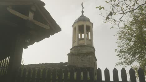 village church bell tower and cross behind lych gate picket fence