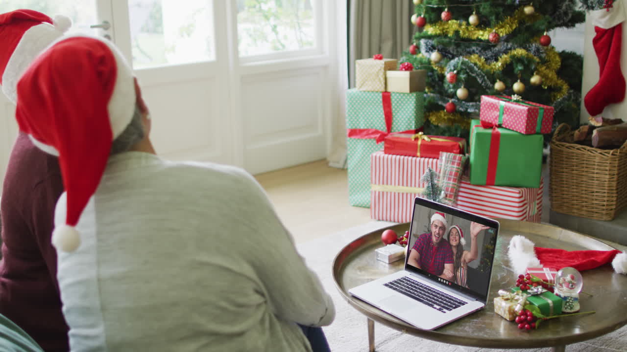 dos amigas mayores diversas que usan una computadora portátil para una videollamada de navidad con una pareja en la pantalla