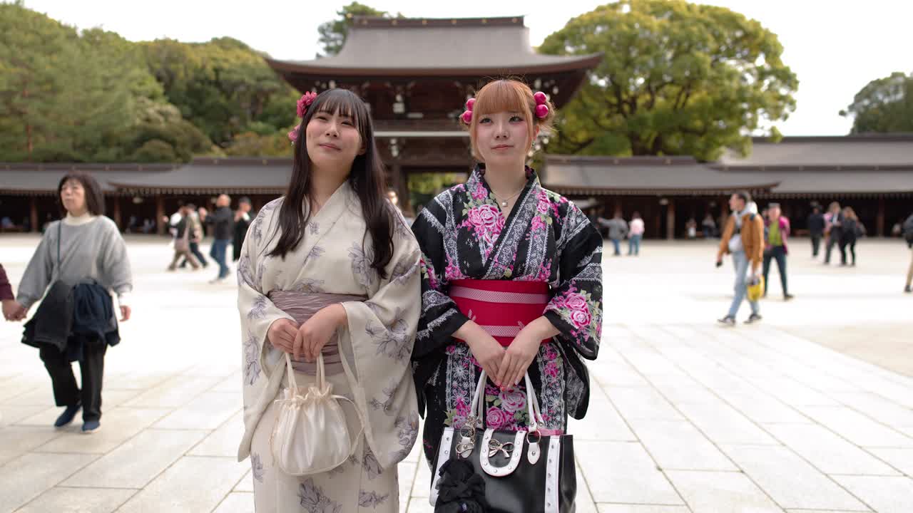 Due donne che indossano kimono floreali si trovano in un cortile davanti a un tradizionale portale di santuario giapponese.