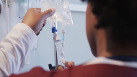 african american female doctor checking drip in hospital room, slow motion