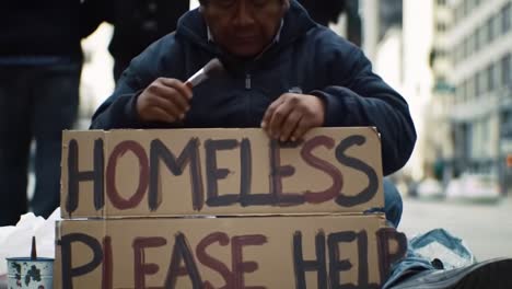 a man sits on the sidewalk in a busy city, holding a sign that reads homeless please help. foot traffic surrounds him as people go about their day.