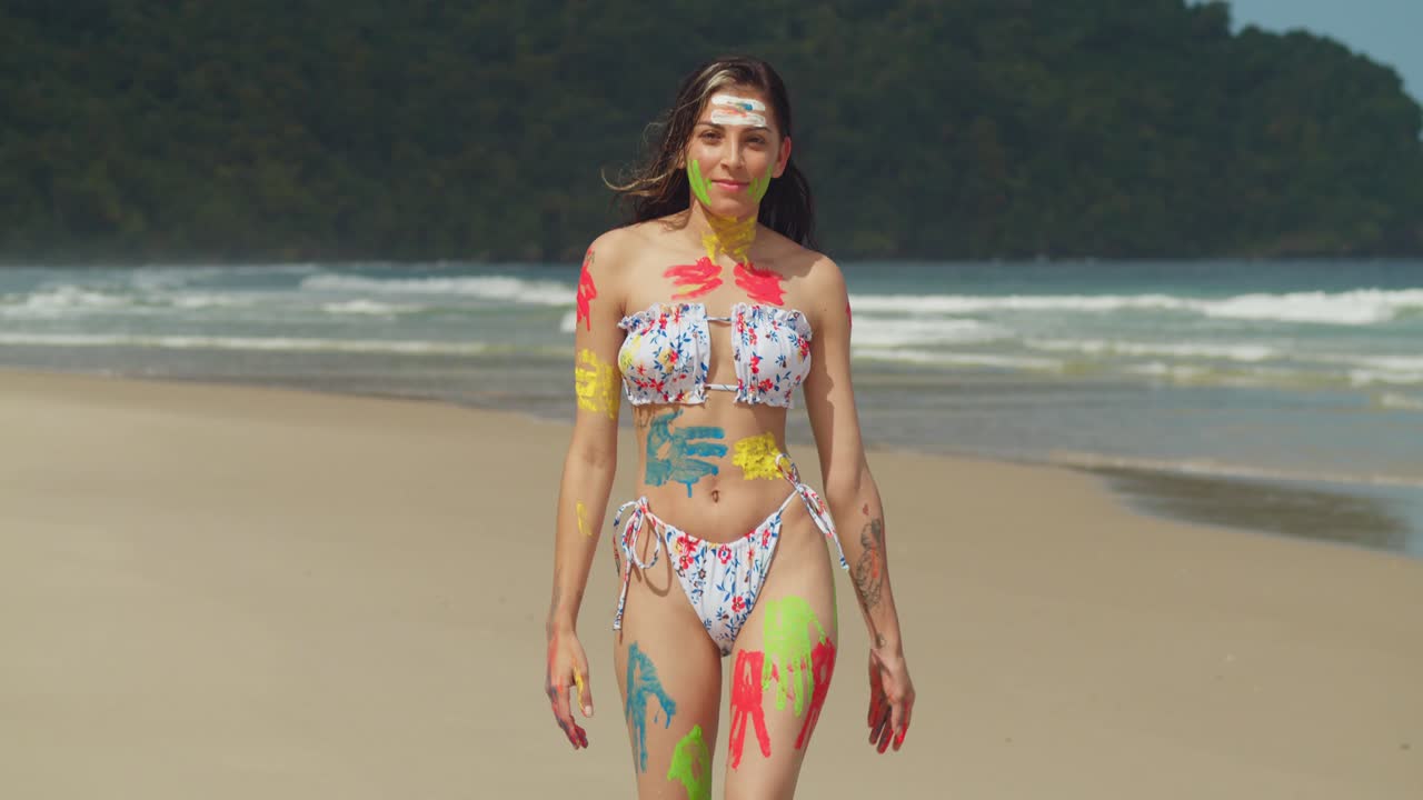 On a sunny day in the Caribbean, a girl adorned in body paint and a bikini walks along a white sand beach