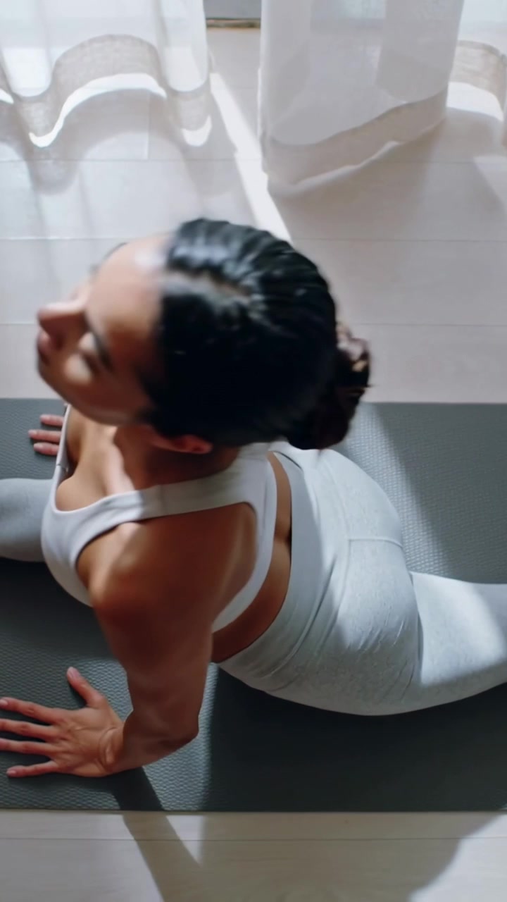 Vertical video: Starting prone, yogi in white set pressing hands, lifting chest on mat by window