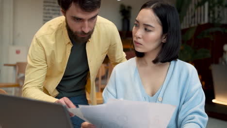 an business woman showing documents on paper and on her laptop to a partner at a meeting in a coffe shop