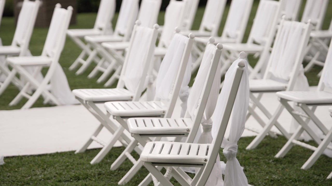 Filas de sillas plegables blancas con decoración de tela, dispuestas al aire libre para un evento.