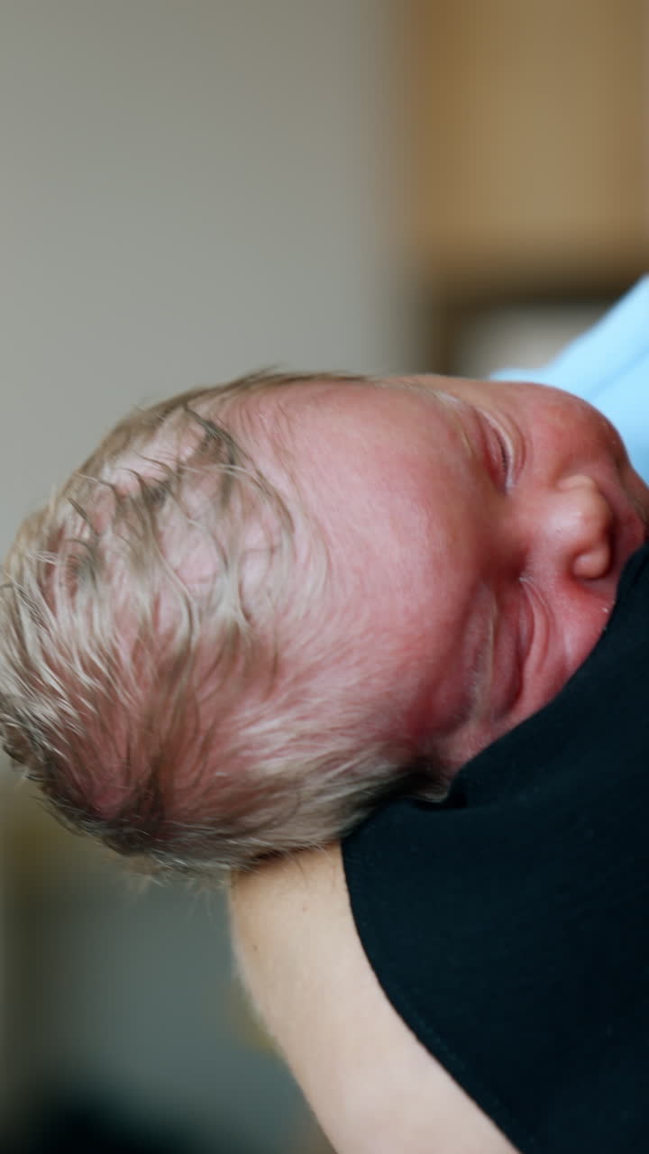 Blond head of a tiny sleeping newborn on mom's arm. Unrecognized mother waving her baby. Close up. Blurred backdrop. Vertical video