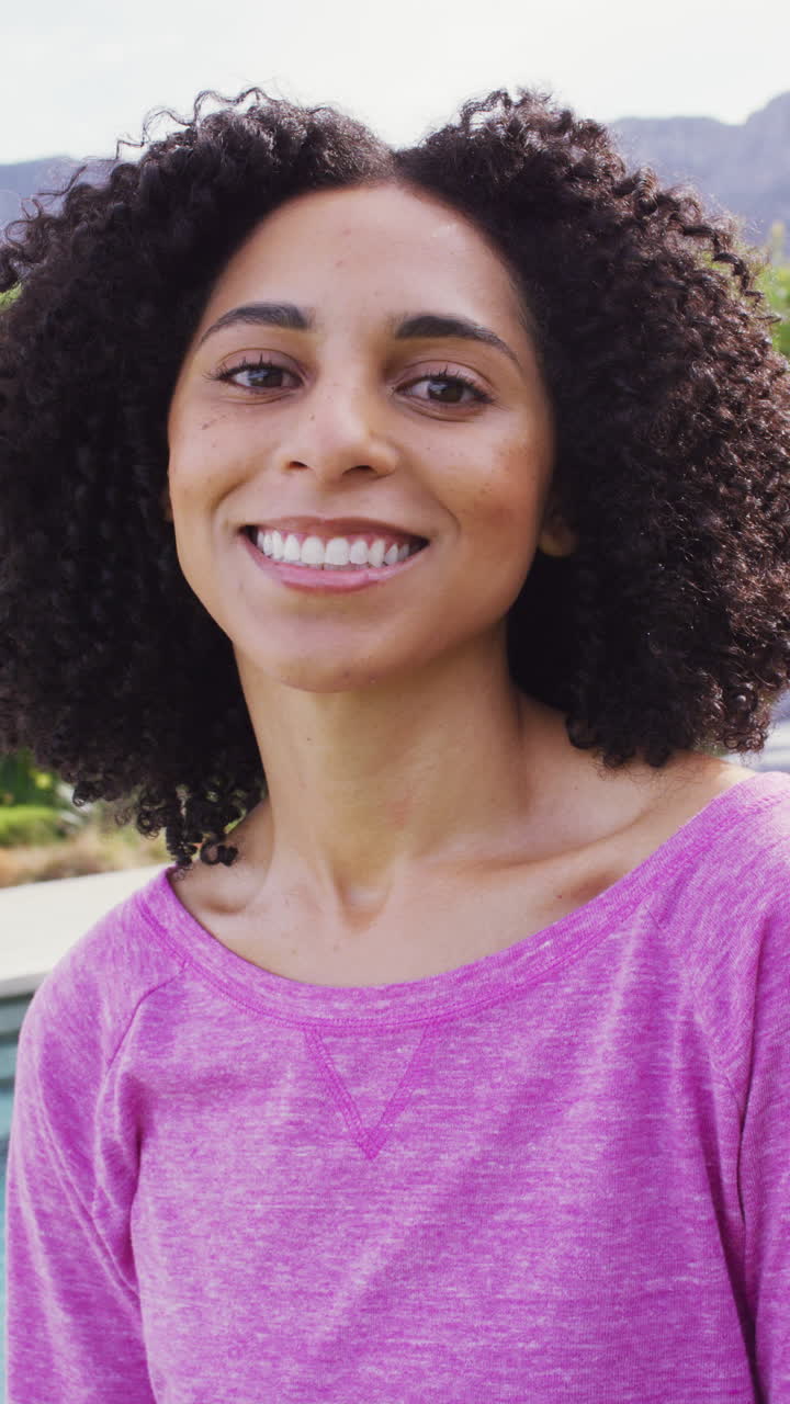 retrato de video vertical de una mujer biracial sonriendo a la cámara al aire libre en el jardín