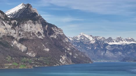 Panning-view-over-calm-blue-water-of-Lake-Walen,-surrounded-by-tall-snowy-mountains-of-the-Alps,-in-Switzerland