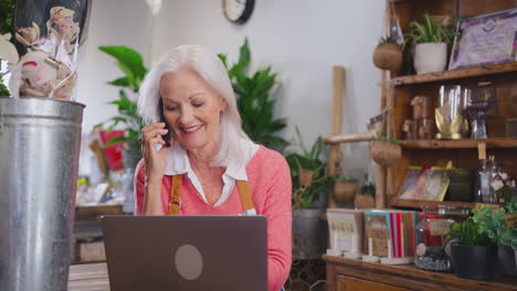 propietaria de una tienda de flores con una computadora portátil hablando por teléfono móvil