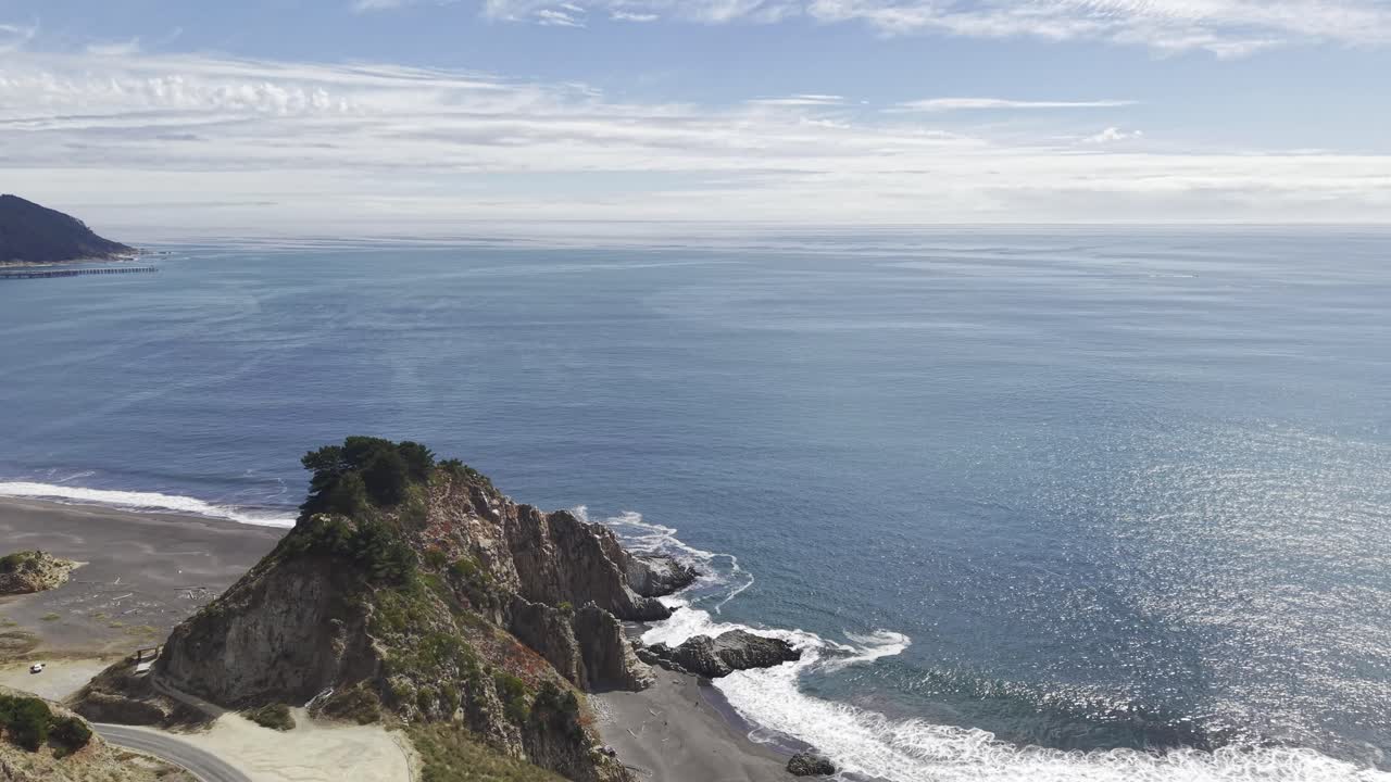 Primo piano e orbita attorno a una formazione rocciosa, Piedra del Elefante, sopra una costa di sabbia scura con moto ondoso e luccichio del sole sul mare sotto nuvole sparse. Constitucion, Cile, 4K.