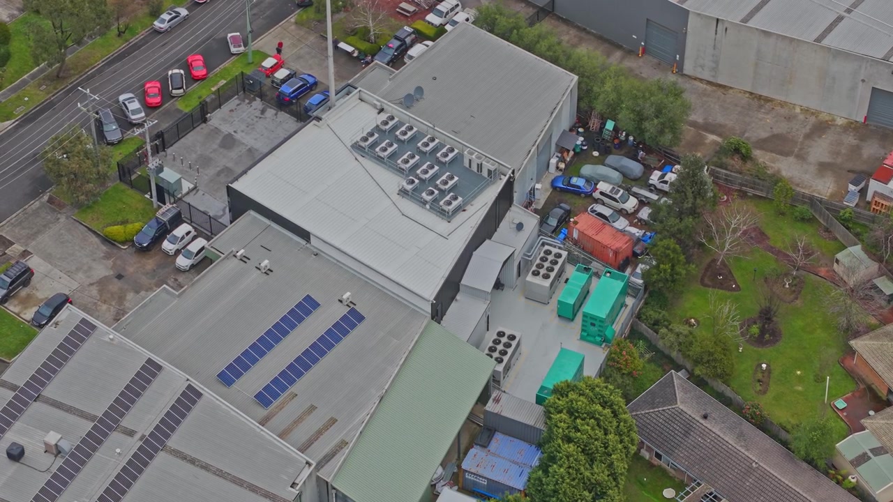 Droneoptagelser viser et højteknologisk datacenter fra oven, med solpaneler, HVAC-enheder, levende grønne generatorer og et sikkert bylayout under overskyet dagslys