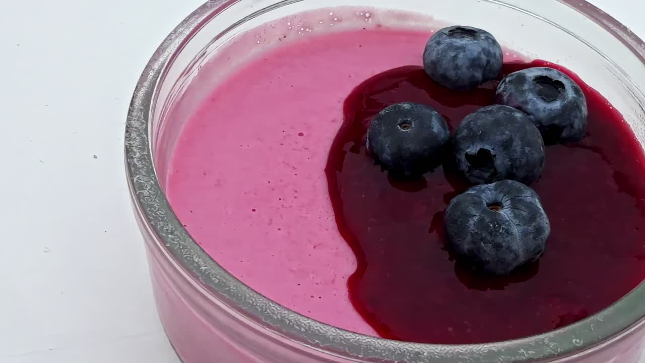 Glass bowl with pink mousse, berry sauce and fresh blueberries as dessert topping