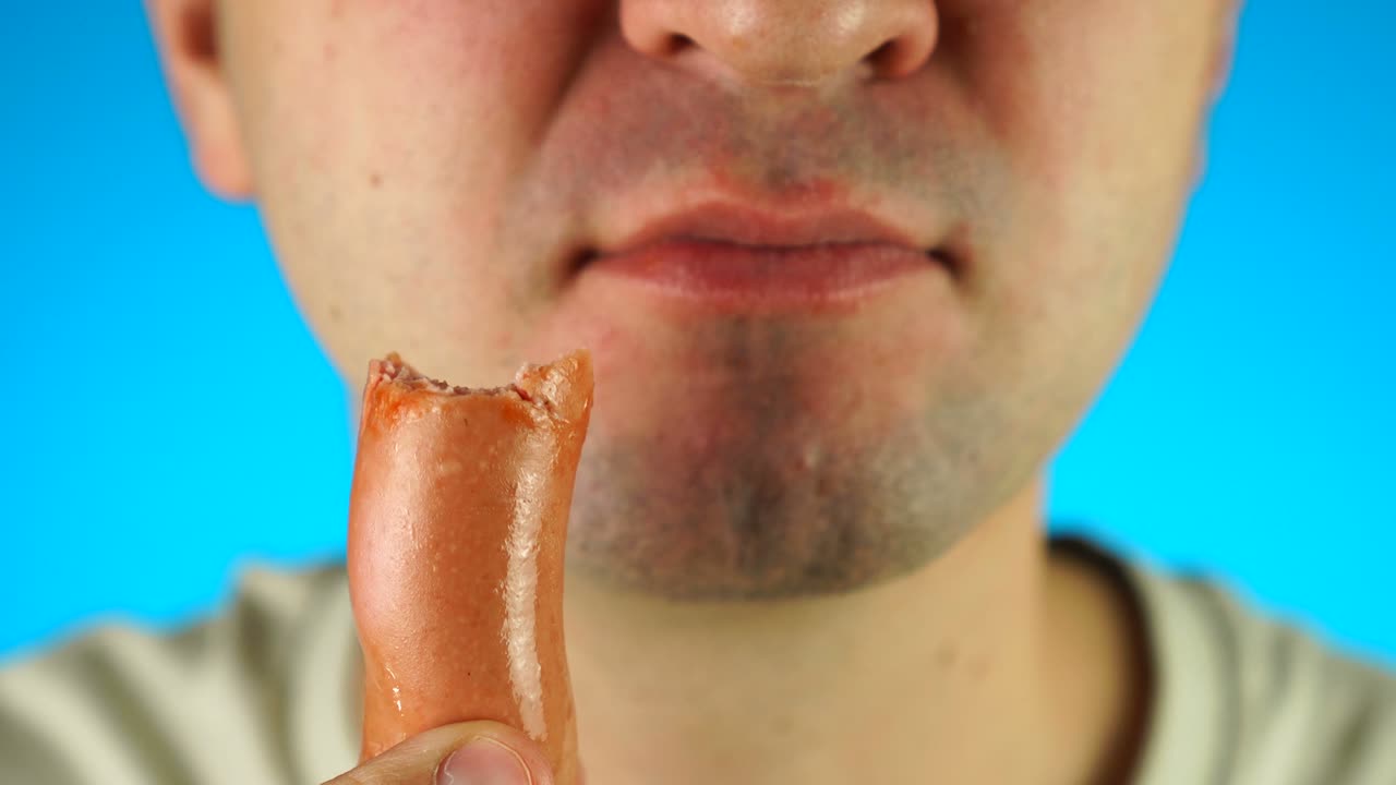 Man biting and eating sausage. Close up of lower half male face, eating meat