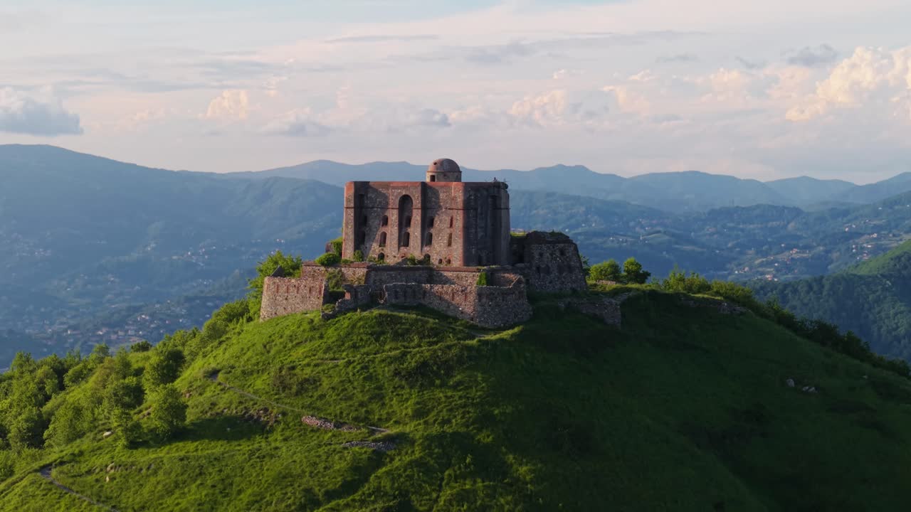 Ancient fort atop a hill in Italy, with surrounding greenery and distant mountains