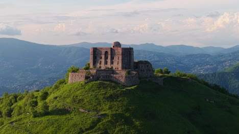 ancient fort atop a hill in italy, with surrounding greenery and distant mountains