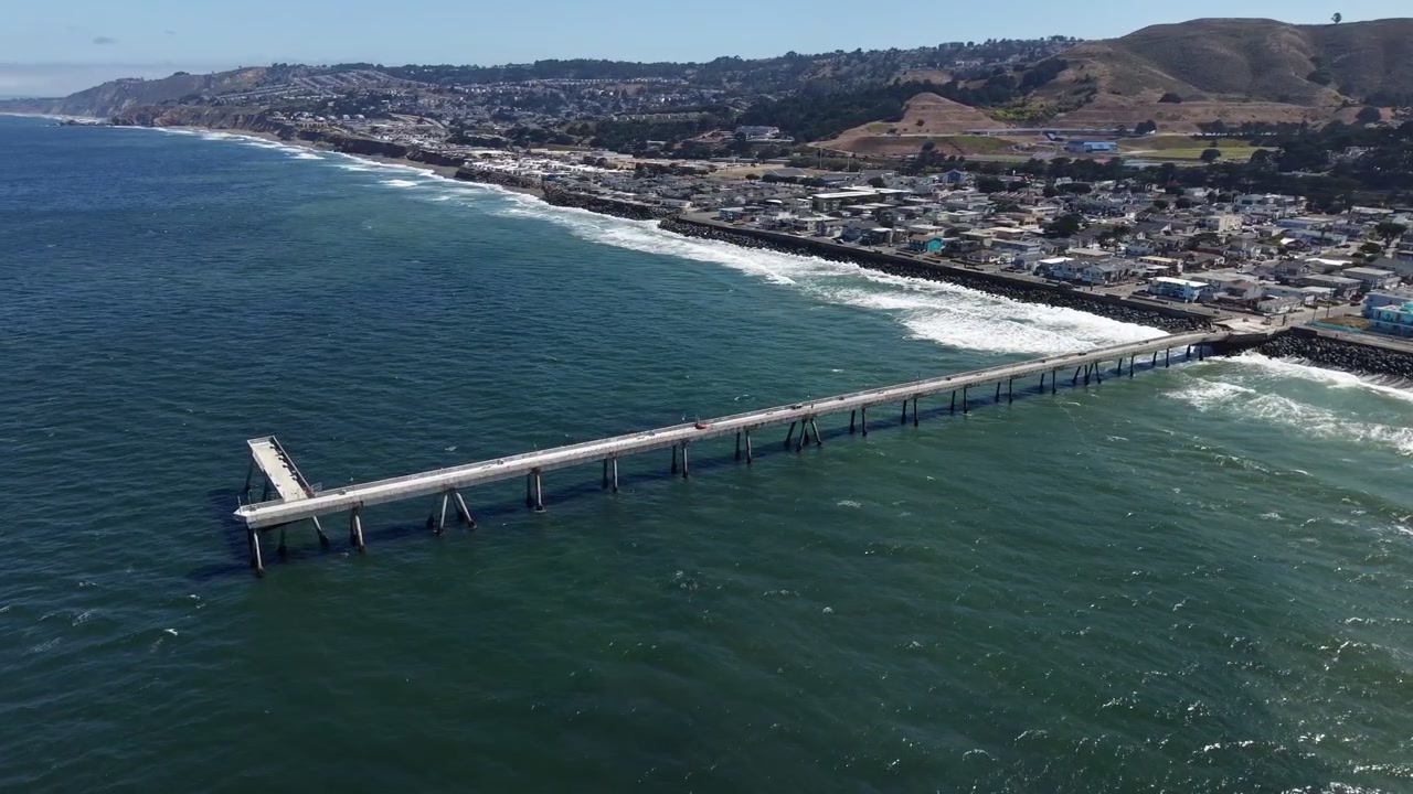 Toma matutina con dron sobre el Océano Pacífico a lo largo del Muelle Municipal de Pacifica, revelando la hermosa costa y la ciudad de Pacifica, California, en un día soleado.