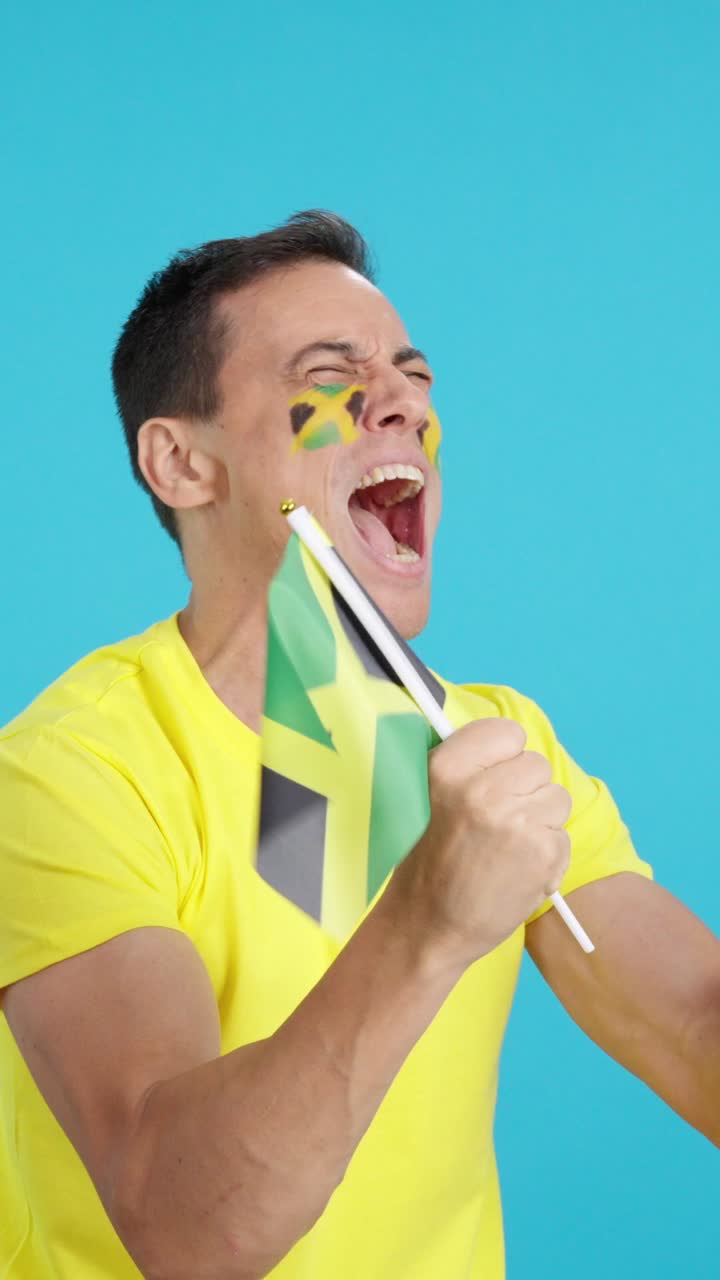 Man cheering for Jamaica waving a national flag looking away