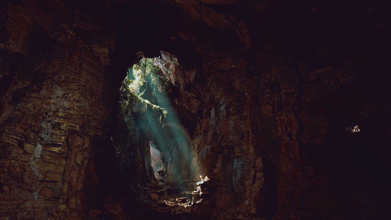 Light beams shine through an opening in a dark cave during midday
