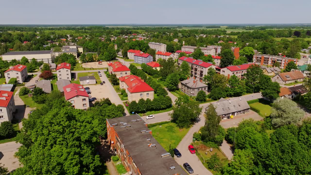 Cinematic aerial of Aizpute townscape featuring rooftops and summer greenery