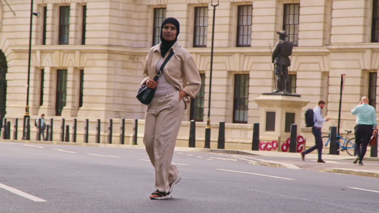 Muslim Businesswoman Wearing Hijab With Modern Business Suit Crossing Road Walking To Work Past City Office Buildings
