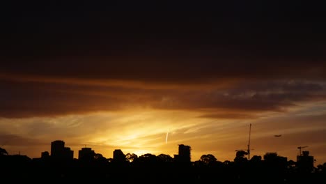 the silhouette of a plane coming in to land behind a cityscape, during a vibrant and beautiful sunset