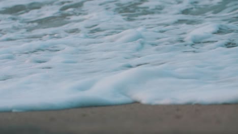 Waves-crashing-on-the-shore,-close-up,-macro-view-of-foamy-waves-at-the-beach-in-slow--motion