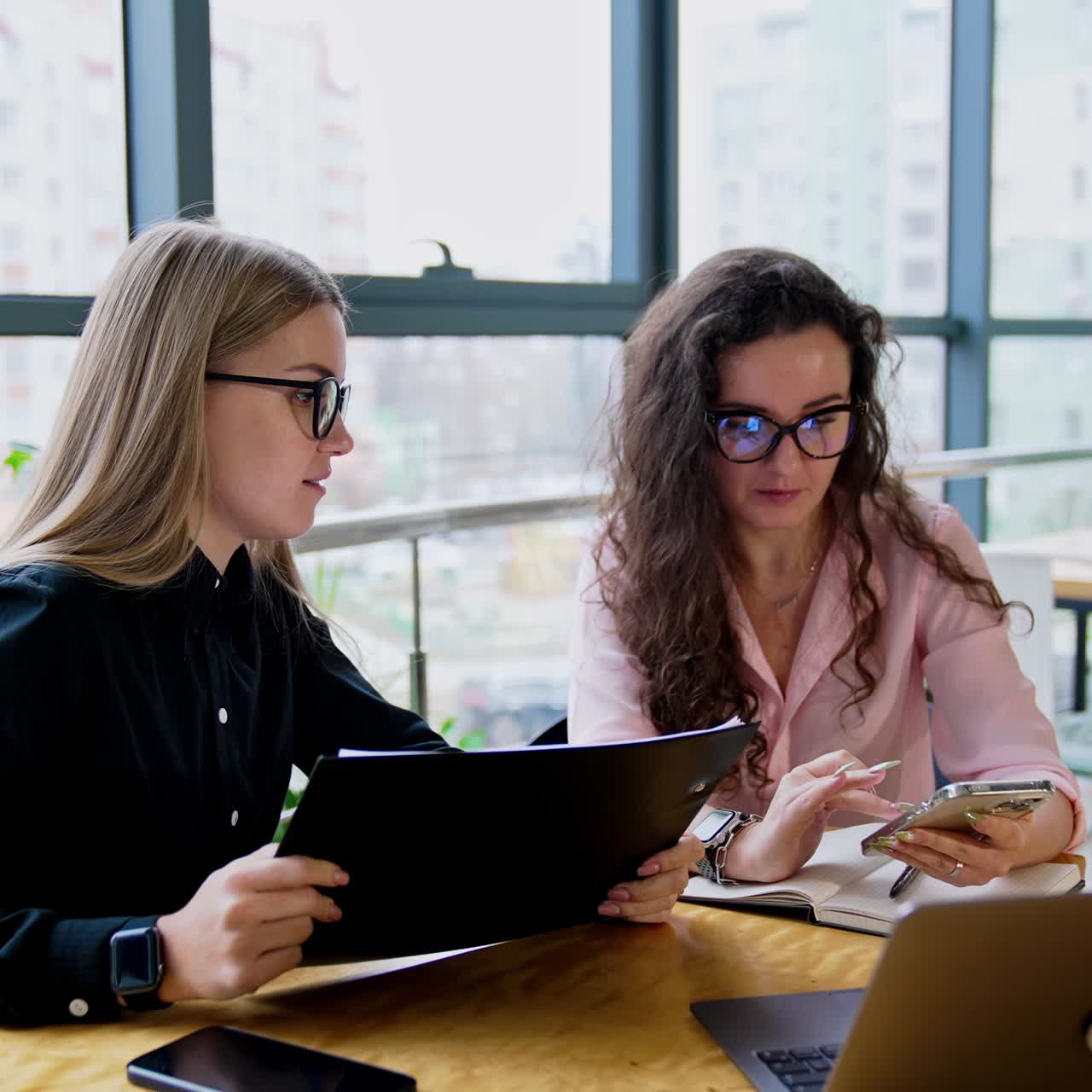 Female coworkers wearing glasses communicate at work. Colleagues using modern technologies for business