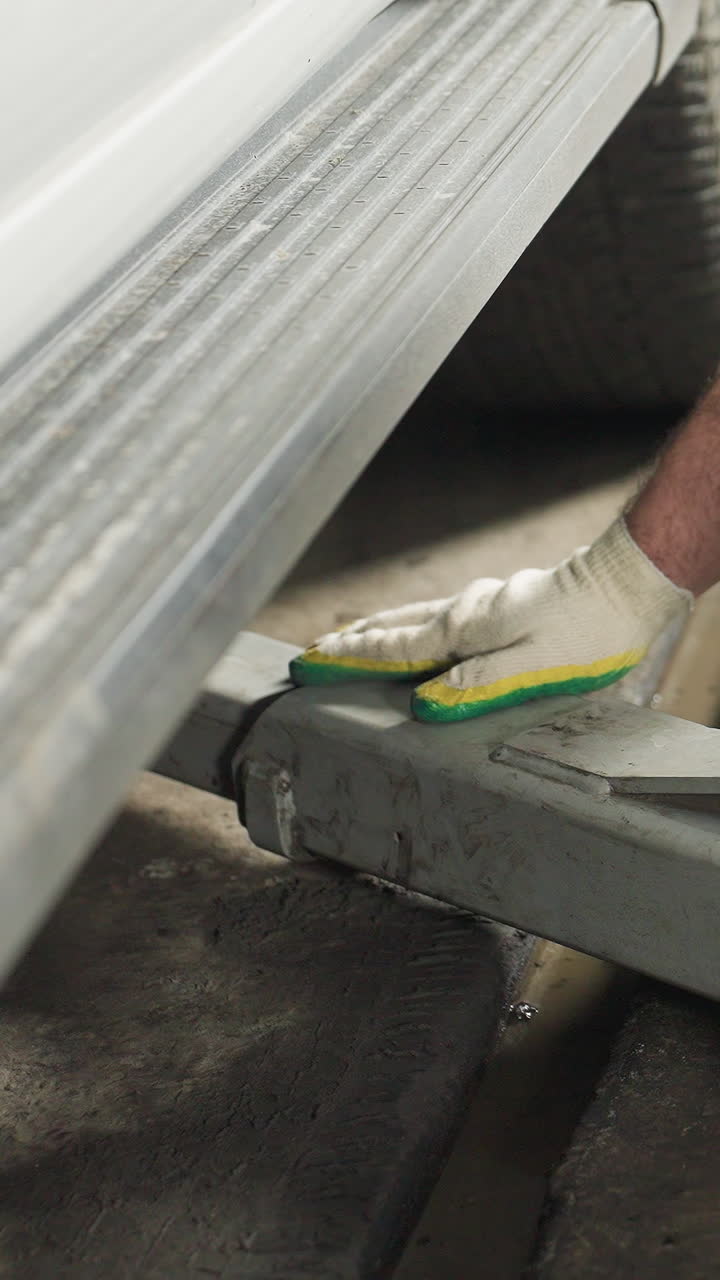Close-up of a mechanic's hand in gloves positioning a car jack under a vehicle next to a blue lift in a well-equipped garage, preparing for maintenance work