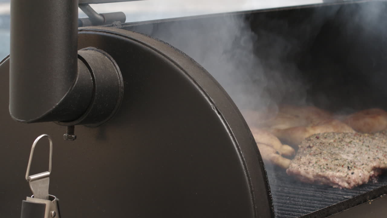 Pan to BBQ pit smoker lid being opened in slow motion, reveals pork ribs and chicken thighs