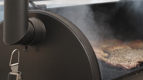 pan to bbq pit smoker lid being opened in slow motion, reveals pork ribs and chicken thighs