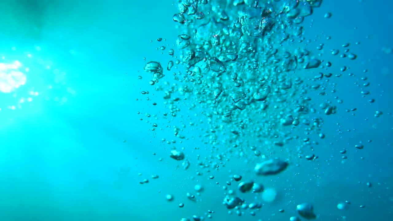 los rayos de luz del sol que brillan desde arriba vienen a través de la profunda agua azul del océano cristalino causando un hermoso reflejo de la iluminación del agua cortina con burbujas de aire que se elevan a la superficie