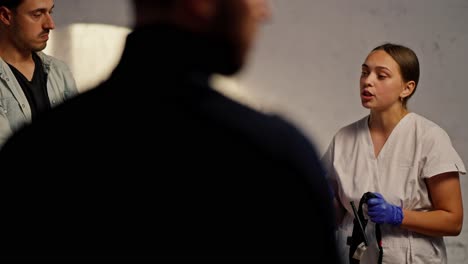 shooting behind the shoulders: a professional female doctor in a white medical uniform conducts medical training and informs the public about the rules for first aid against a white wall