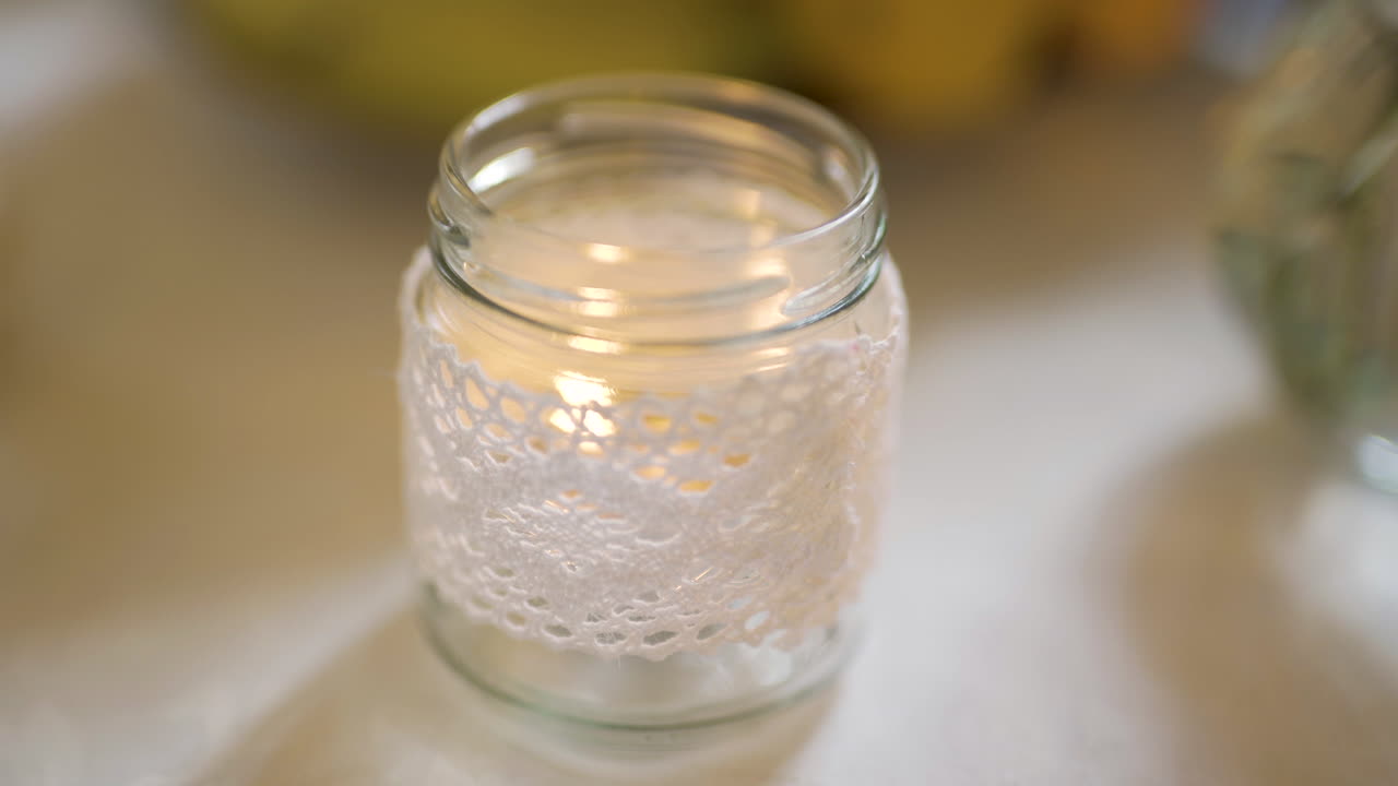 Bougie vacillante dans un bocal en verre décoré de dentelle