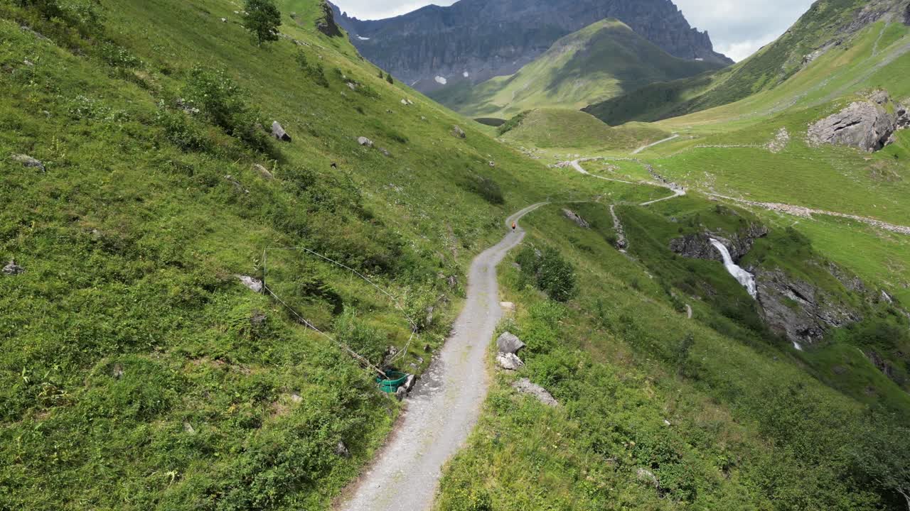 vista aérea un dron sigue un camino de montaña natural hecho con grava, verdes prados de los alpes suizos