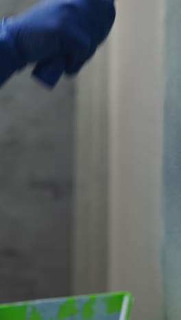 african-american worker in gloves applies paint on wall with roller in living room close side view. black man decorates new apartment. repairing process