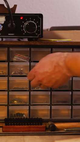 worker seeks right metal rivets in organizer with small drawer in workshop closeup. craftsman chooses nails for work in studio. supplies and tools