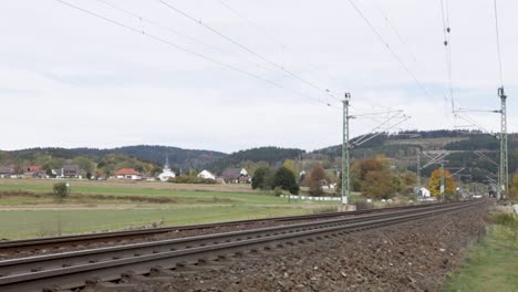 red deutsche bahn train approaching on tracks through a rural landscape with houses and church in the background, daytime