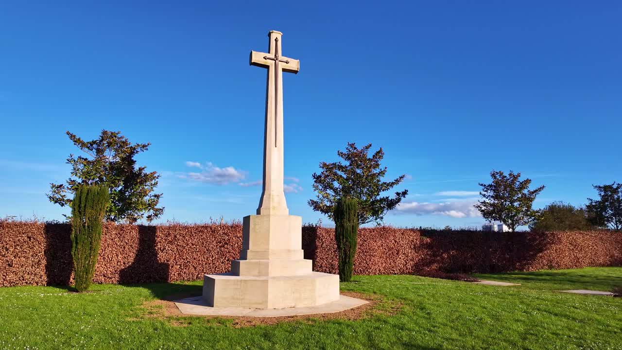 Detailed view of the war memorial within the cemetery, surrounded by graves and spring foliage.