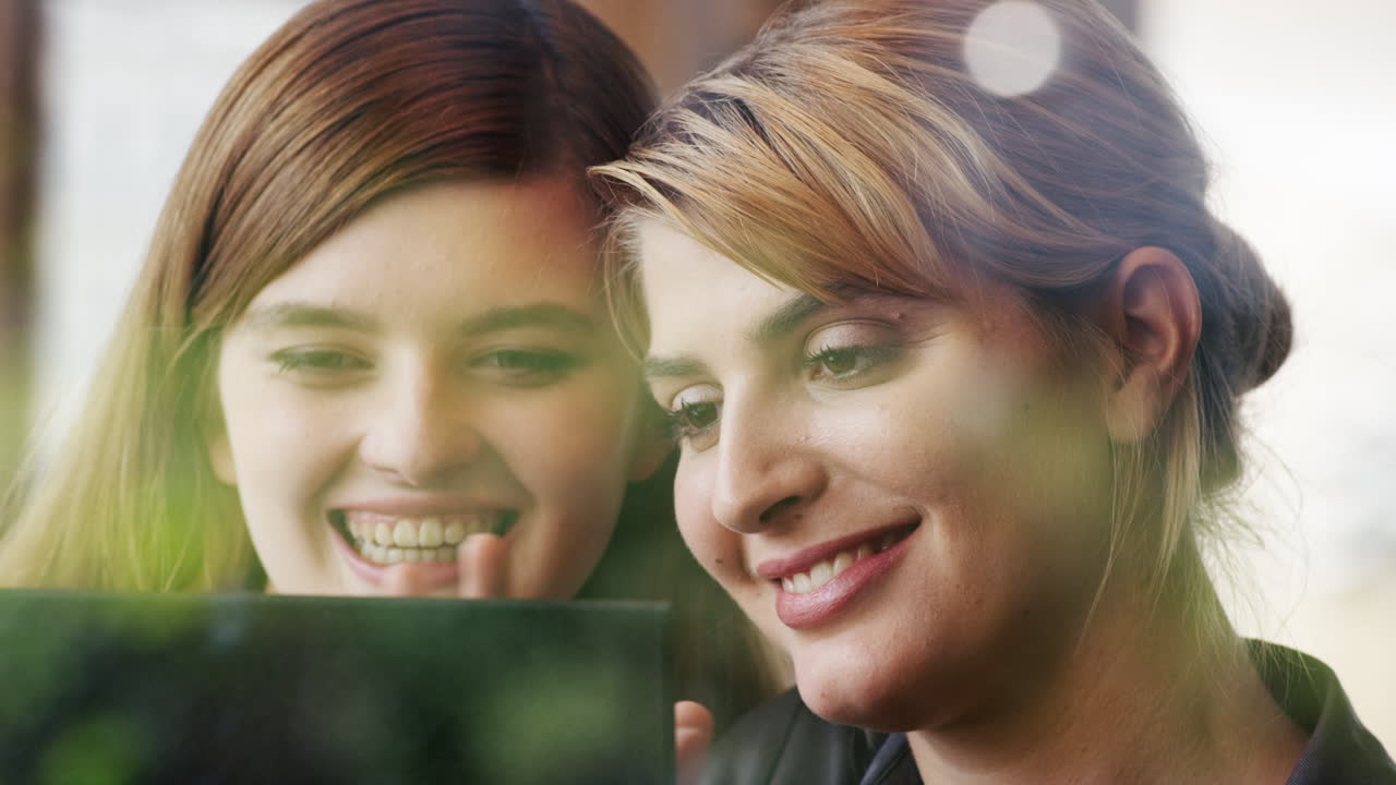 dos mujeres usando una tableta digital bebiendo café en una cafetería
