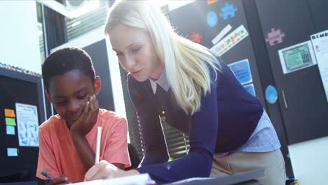 Teacher-helping-schoolboy-with-his-homework-in-classroom