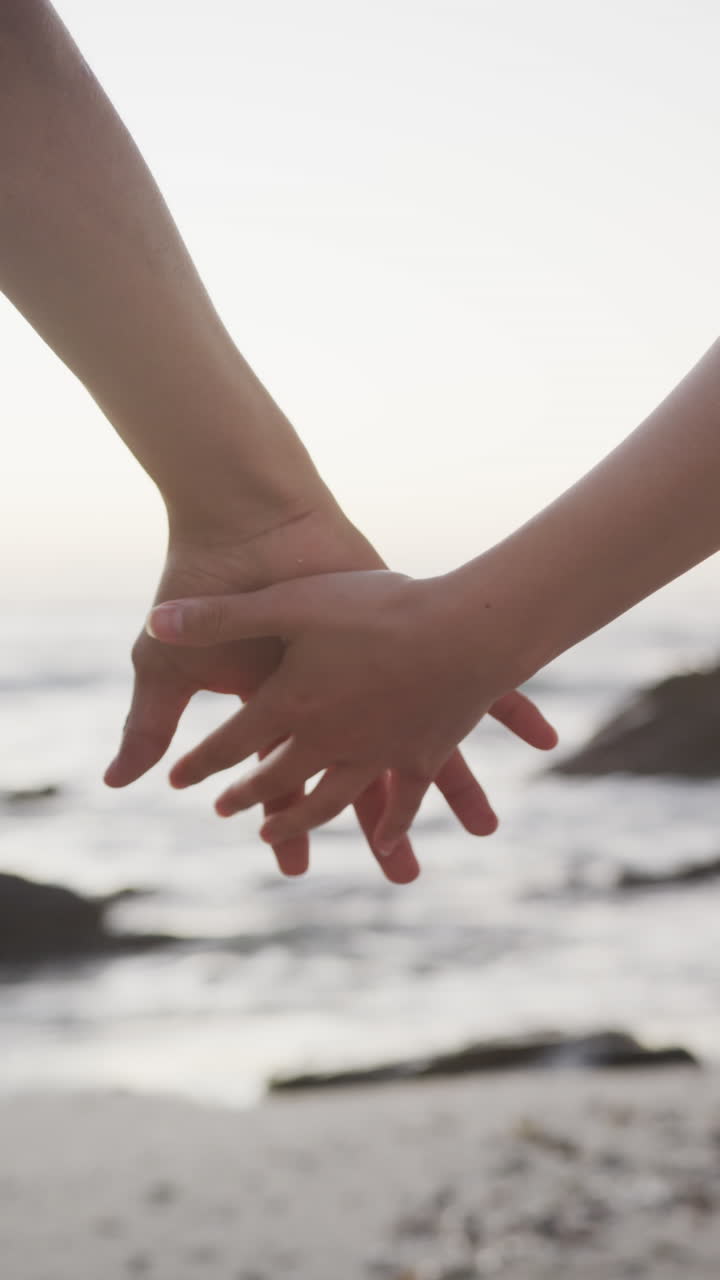 Vertical video of biracial couple holding hands at beach, in slow motion