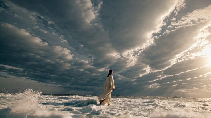 Una scena video drammatica cattura una persona con una veste fluente che cammina sull'acqua sotto un cielo nuvoloso