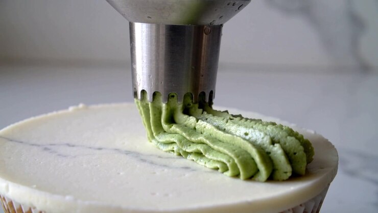 Pressing piping tip extruding green icing ribbon on kitchen counter, decorating cupcake