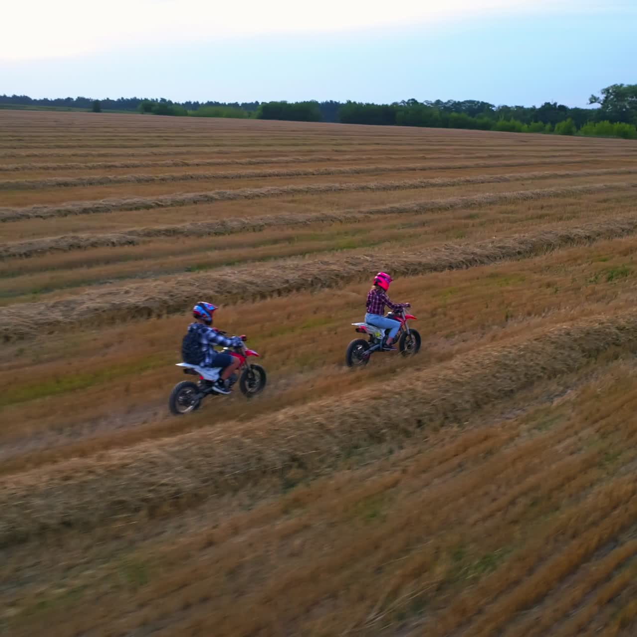 Two people riding motorbikes in the countryside. Girl in pink helmet riding first followed by her boyfriend. Top view